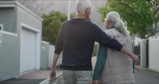 Altes Paar beim gemeinsamen Spaziergang in der Nachbarschaft mit Umarmung, Lächeln oder Liebe am Morgen von hinten. Entspannen Sie sich im Rentenurlaub, alter Mann und glückliche Frau umarmen sich auf der Straße für einen ruhigen, gesunden Spaziergang im Freien - Filmmaterial, Video
