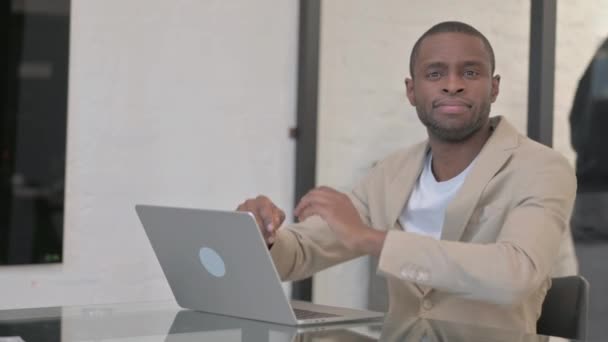 Africano americano homem sorrindo para câmera enquanto trabalhava no laptop no escritório - Filmagem, Vídeo