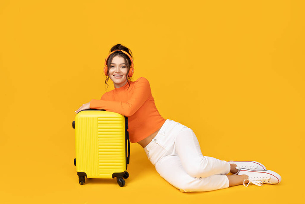 Una joven en auriculares y con una maleta amarilla - Foto, imagen