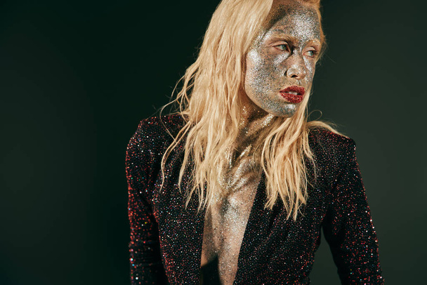 portrait of blonde woman with glitter on face and body posing in shiny dress on black backdrop - Photo, Image