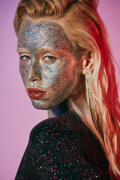 portrait of striking blonde woman with glitter makeup and shiny dress posing on pink backdrop - Photo, Image