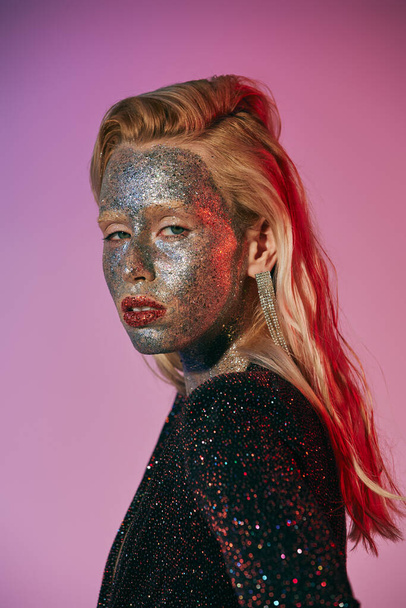 portrait of striking and blonde woman with glitter makeup and shiny dress posing on pink backdrop - Photo, Image