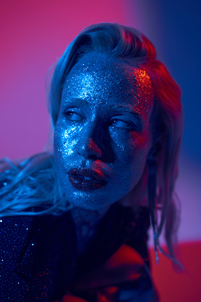 muotokuva kaunis blondi nainen glitter kasvot ja kiiltävä asu poseeraa neon tausta - Valokuva, kuva
