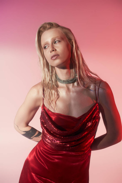 tattooed blonde woman in red dress with sequins and luxury jewelry posing on pink background - Φωτογραφία, εικόνα