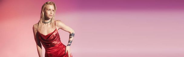 beautiful woman in stylish red dress on pink backdrop with hand on hip looking away, banner - Photo, Image