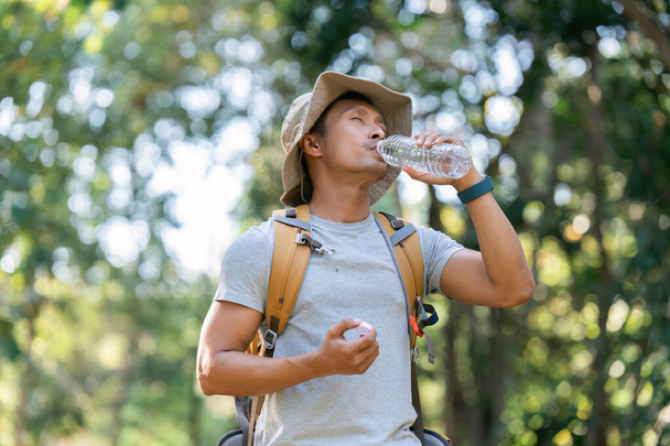 Young man backpacker traveling alone in forest. Attractive male traveler drinking water while walking in nature wood during holiday vacation trip. - Photo, Image