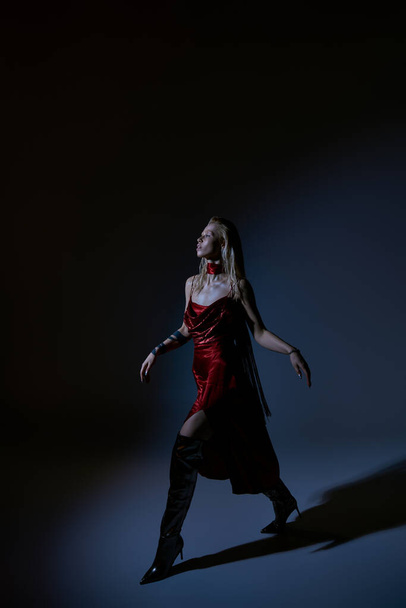 gyönyörű nő piros szexi ruha tetoválás pózol mozgásban sötét háttér és elnézett - Fotó, kép