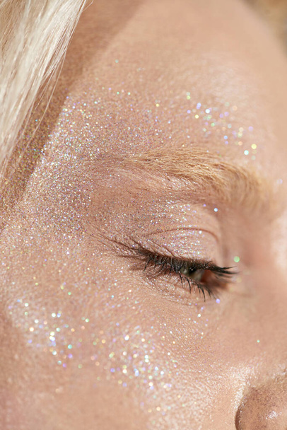 close up of young woman with beautiful green eye and glitter on her face looking away, highlighter - Foto, Bild
