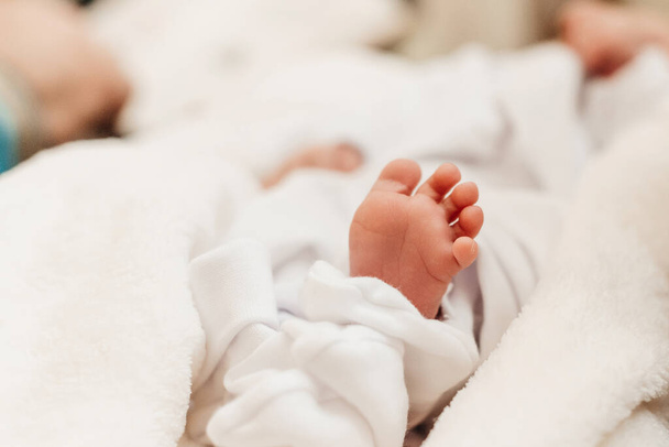 Bir bebeğin küçük bacağı vaftiz sırasında beyaz bir çarşafın üzerinde, yeni doğmuş bir bebek. - Fotoğraf, Görsel