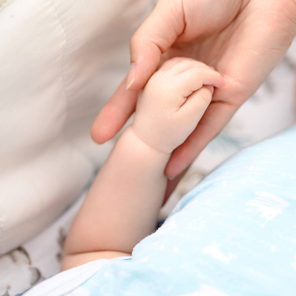 Маленька рука новонародженої дитини крупним планом, мати підтримує дитину. - Фото, зображення