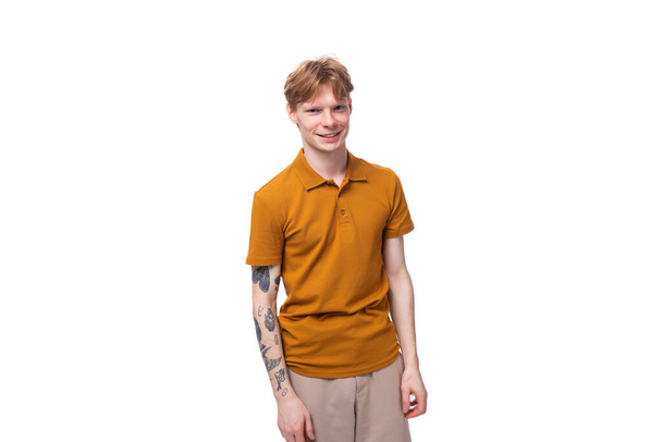 молодий стильний рудий чоловік зі стрижкою та татуюванням на руці одягнений у жовту футболку. - Фото, зображення