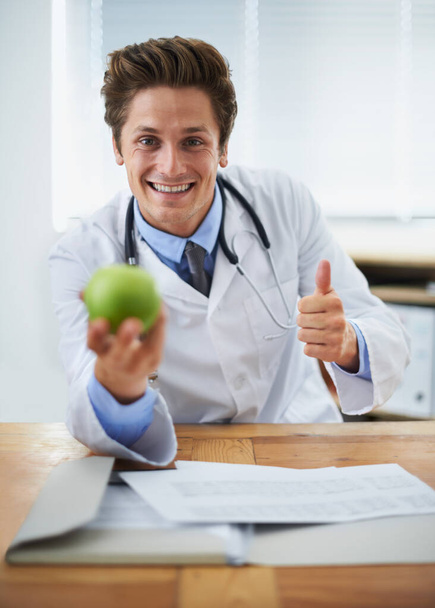 Thumbs up, apple and portrait of man doctor with stethoscope for positive, good and confident attitude. Happy, smile and young healthcare worker with fruit in medical office of hospital or clinic - Photo, Image