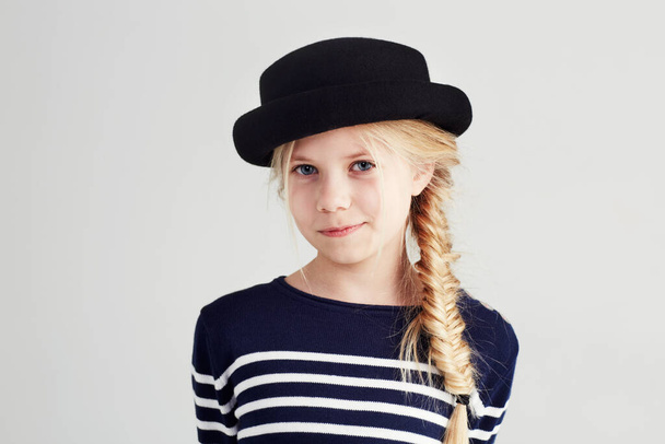 Moda, szczęśliwy i portret dziecka w studio w luźnym, chłodnym i stylowym stroju i kapeluszu. Uśmiech, młodość i młoda dziewczyna dziecko z pozytywnym, dobre i pewne nastawienie do stylu przez białe tło. - Zdjęcie, obraz