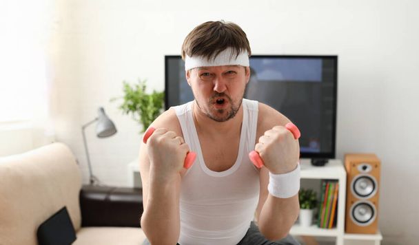 Jovem homem atraente envolvido na aptidão em casa segurando halteres na mão tentando lutar contra o excesso de peso e perda
 - Foto, Imagem