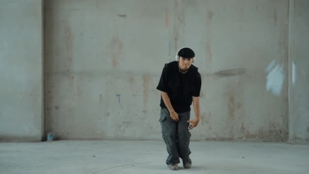 Jóképű hipster gyakorló break tánc közben zenét hallgat fejhallgató cement háttérrel. Mozgókép utcai táncosról, ahogy robottáncol. Kültéri sport 2024. Modern tánc. hiphop. - Felvétel, videó