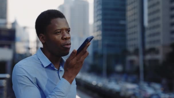 Ernsthafter afroamerikanischer Geschäftsmann nimmt Sprachnachrichten auf, während er während der Pause draußen in der Nähe des Bürobezirks steht. Junger Geschäftsmann liest Befehle auf seinem Smartphone für KI-Suche - Filmmaterial, Video