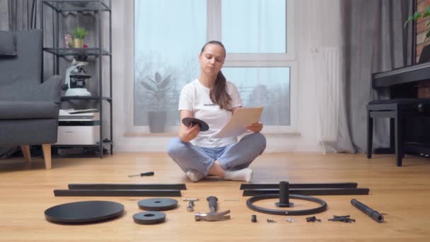 Parçaların önünde oturan bir kadın dikkatlice talimatlara bakar ve mobilyaları monte etmek için gerekli elementi seçer.. - Video, Çekim