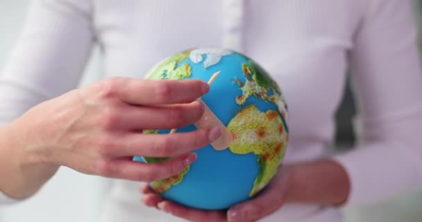 Vrouw plaatst zelfklevende strips op Aarde model. Vrouw hecht pleisters op wereldbol symboliseert zorg voor de planeet en de nadruk leggen op milieu-genezing - Video