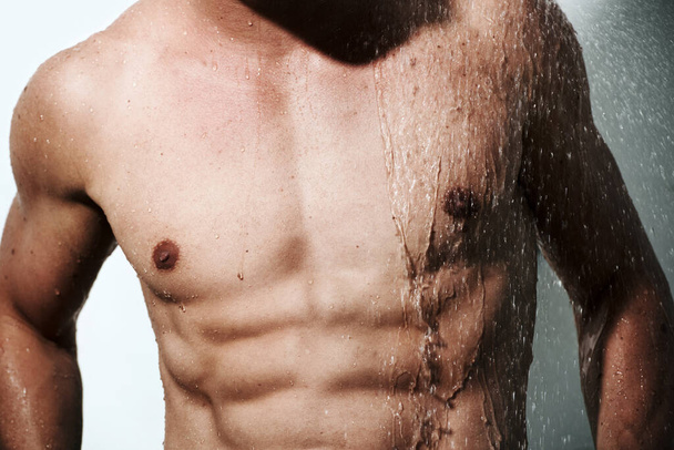 Closeup, muscular man or wet with body, hygiene or fitness with abs, routine or wellness on studio background. Person, guy or model with water, bodybuilder or cleaning with energy, chest or aesthetic. - Photo, Image