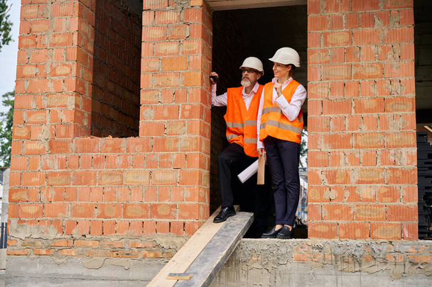 Site manager and foreman with architectural drawing in hand standing in doorway of unfinished house - Foto, Bild