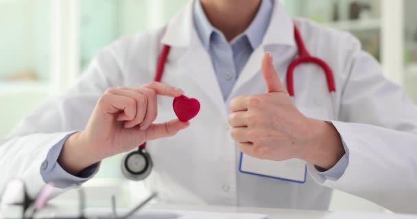 Lekarz rodzinny trzyma serce zabawki podkreślając znaczenie zdrowia serca. Lekarz używa gestu kciuka w górę, aby pokazać pozytywny aspekt zdrowia układu krążenia - Materiał filmowy, wideo