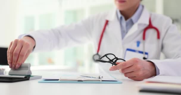 A háziorvos szemüveget tart a kezében, hogy átnézze az orvosi feljegyzéseket. Professzionális orvos fókuszált kifejezéssel bélyegzőt helyez az orvosi dokumentumra - Felvétel, videó