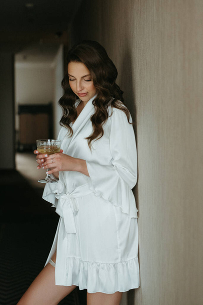 朝,白ワインのグラスとホテルの廊下のバスローブで茶色の髪の少女 - 写真・画像