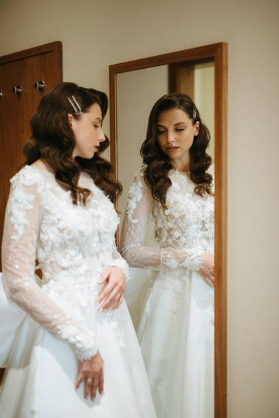 chica de cabello castaño se pone un vestido de novia en una habitación de hotel por la mañana - Foto, Imagen