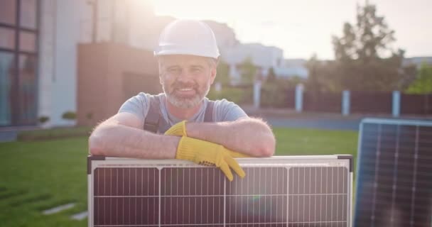 再生可能エネルギー企業で働いている白人男性. ソーラーパネルで流れるプロの請負業者と笑顔. 太陽電池パネルを設置する男性技術者. 代替エナジーソース. - 映像、動画
