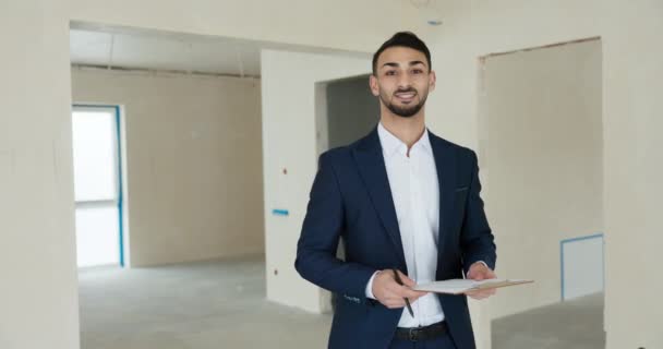 Orta Doğulu genç emlak yöneticisi müşterilerini karşılıyor. Yeni modern bina binasında müşterileri kameraya el sallayarak merhaba diyor.. - Video, Çekim