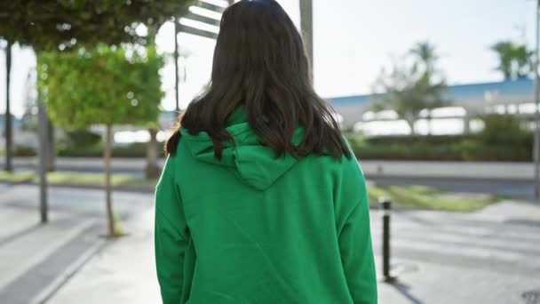 Een jonge vrouw met een groene capuchon die zelfverzekerd buiten staat in een stedelijke omgeving met gekruiste armen. - Video