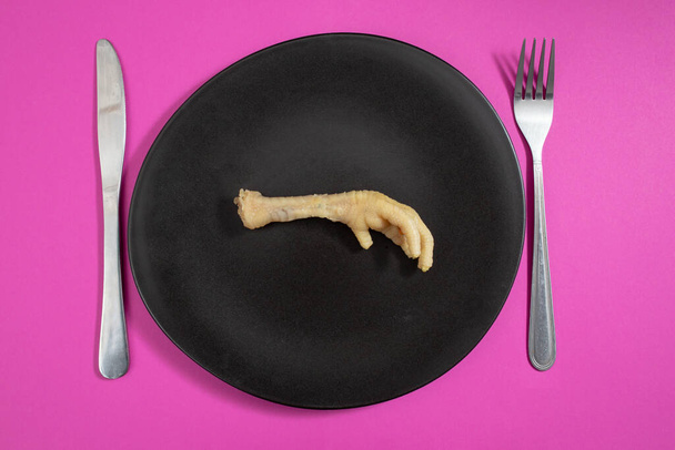 Куриная нога на черной керамической пластине и пурпурном фоне, продовольственный кризис   - Фото, изображение