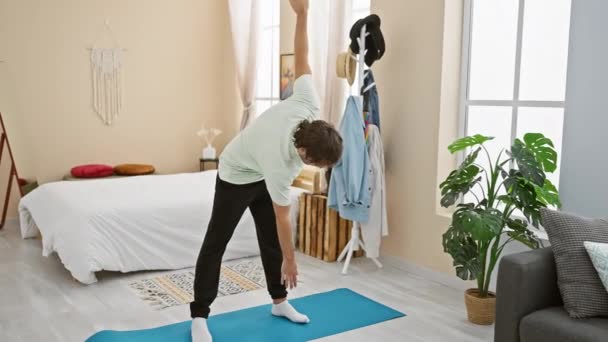Um jovem se estende em um tapete de ioga em seu quarto bem iluminado e acolhedor, incorporando bem-estar e tranquilidade doméstica. - Filmagem, Vídeo