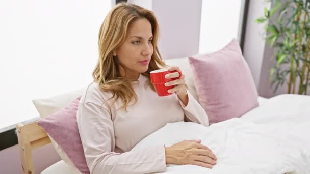 Eine Frau genießt einen morgendlichen Kaffee im Bett, der Entspannung in einer gemütlichen Schlafzimmeratmosphäre schafft. - Filmmaterial, Video