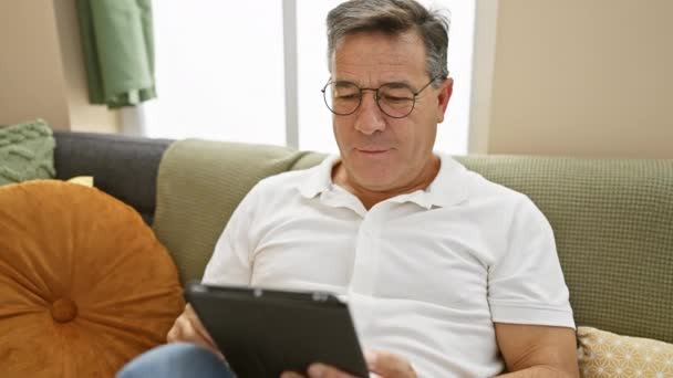 Volwassen man in bril met behulp van tablet op de bank thuis - Video