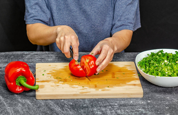 Manos femeninas cortando tomate en tabla de cortar. Camiseta azul, fondo negro. Preparación de ensaladas - Foto, Imagen