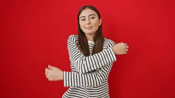 Onnellinen, itsevarma nuori latino nainen raidoissa t-paita halailee itseään, säteilee itsensä rakkautta hehkuva punainen eristetty tausta - Materiaali, video