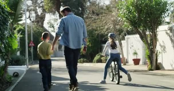 Vanhemmat, lapset ja polkupyörän ratsastaa tyttö, kypärä ja ulkona kadulla kädestä pitäminen. Pyöräily, lapsuus ja ratsastus naapurustossa, sitoutuminen yhdessä ja turvallisuus pojan kanssa, ylpeä ja onnellinen. - Materiaali, video