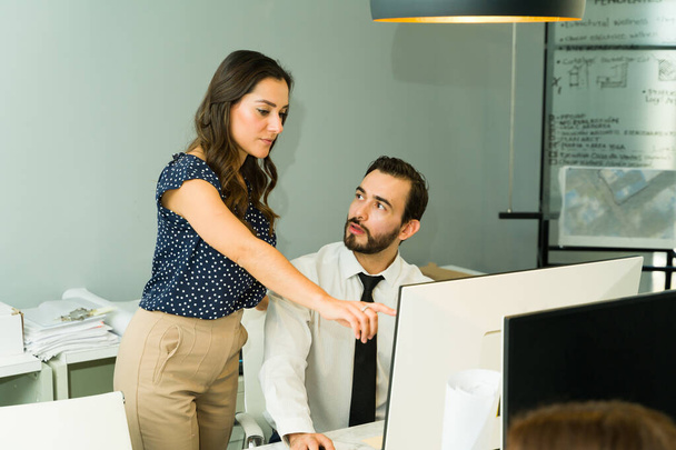 Hispánská žena šéf pomáhá muži s jeho prací a dělat nějaké připomínky, zatímco ukazuje na obrazovce počítače - Fotografie, Obrázek