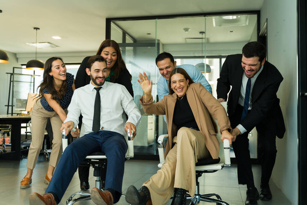 Monipuolinen ryhmä työntekijöitä, joilla on liian hauskaa toimistossa kilpa joitakin tuoleja - Valokuva, kuva