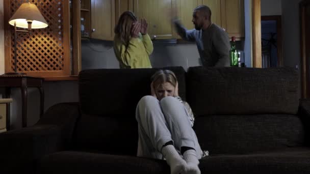 hija se sienta en el sofá con la cubierta de sus oídos, cubriendo sus oídos para no escuchar a sus padres peleas, un par de cosas en la cocina en presencia de un niño, de alta calidad 4k metraje - Metraje, vídeo