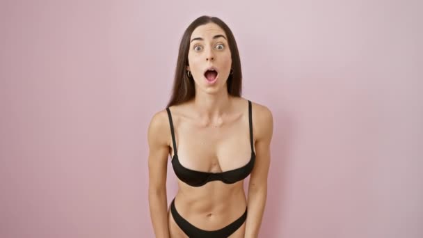 Verbazingwekkende jonge Spaanse vrouw, in prachtige lingerie, draagt een uitdrukking van schok en ongeloof, over roze geïsoleerde achtergrond. - Video
