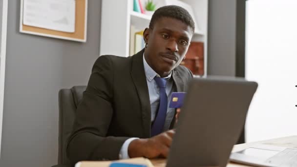 Un hombre negro profesional en traje de negocios usando una tableta en el interior de una oficina con una tarjeta de crédito en la mano. - Metraje, vídeo