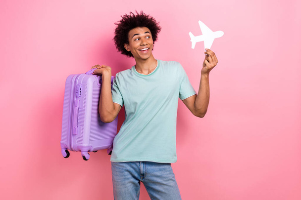 Photo of cool excited guy wear blue t-shirt rising baggage holding paper plane empty space isolated pink color background. - Photo, image