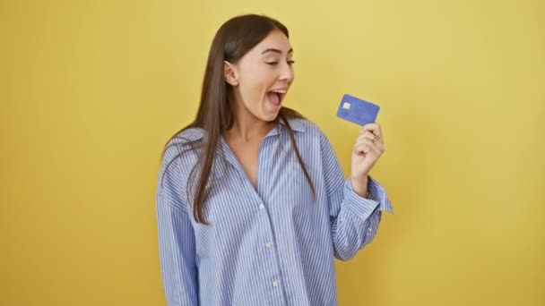 Young beautiful hispanic woman holding credit card screaming proud, celebrating victory and success very excited with raised arms over isolated yellow background - Footage, Video