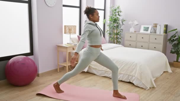 Een jonge vrouw oefent yoga in een lichte slaapkamer, oefenen op een roze mat in de buurt van een paarse oefenbal. - Video