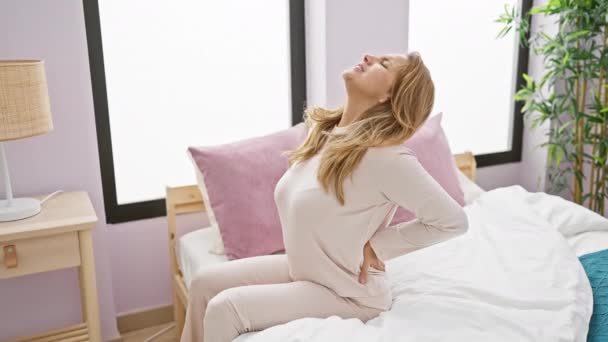 Egy fiatal nő hátfájást tapasztal jól megvilágított hálószobájában, ami kényelmetlenséget és otthon a wellness iránti igényt közvetíti.. - Felvétel, videó