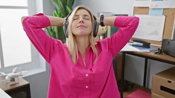 Eine Frau entspannt sich mit Kopfhörern in einem modernen Büro mit hellen Fenstern und Aufbewahrungsboxen. - Filmmaterial, Video