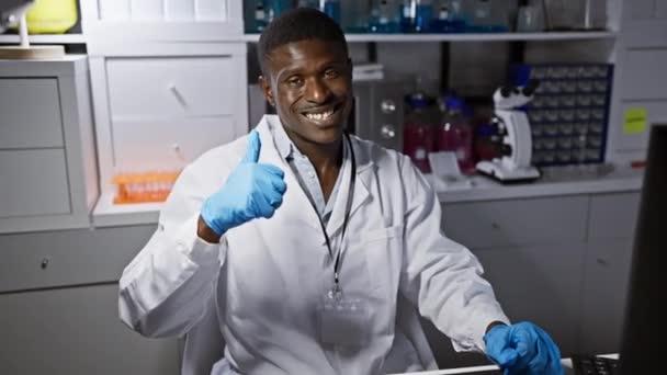 Веселий афроамериканський вчений в рукавичках дає знак "гак", випромінюючи позитивізм і впевненість в лабораторії, аромат успіху навколо! - Кадри, відео