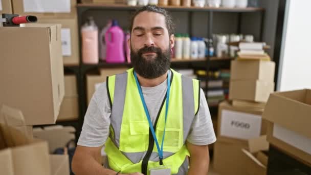 Hombre hispano con barba en el almacén con chaleco de seguridad sosteniendo el corazón rojo, retratando trabajo y cuidado. - Metraje, vídeo